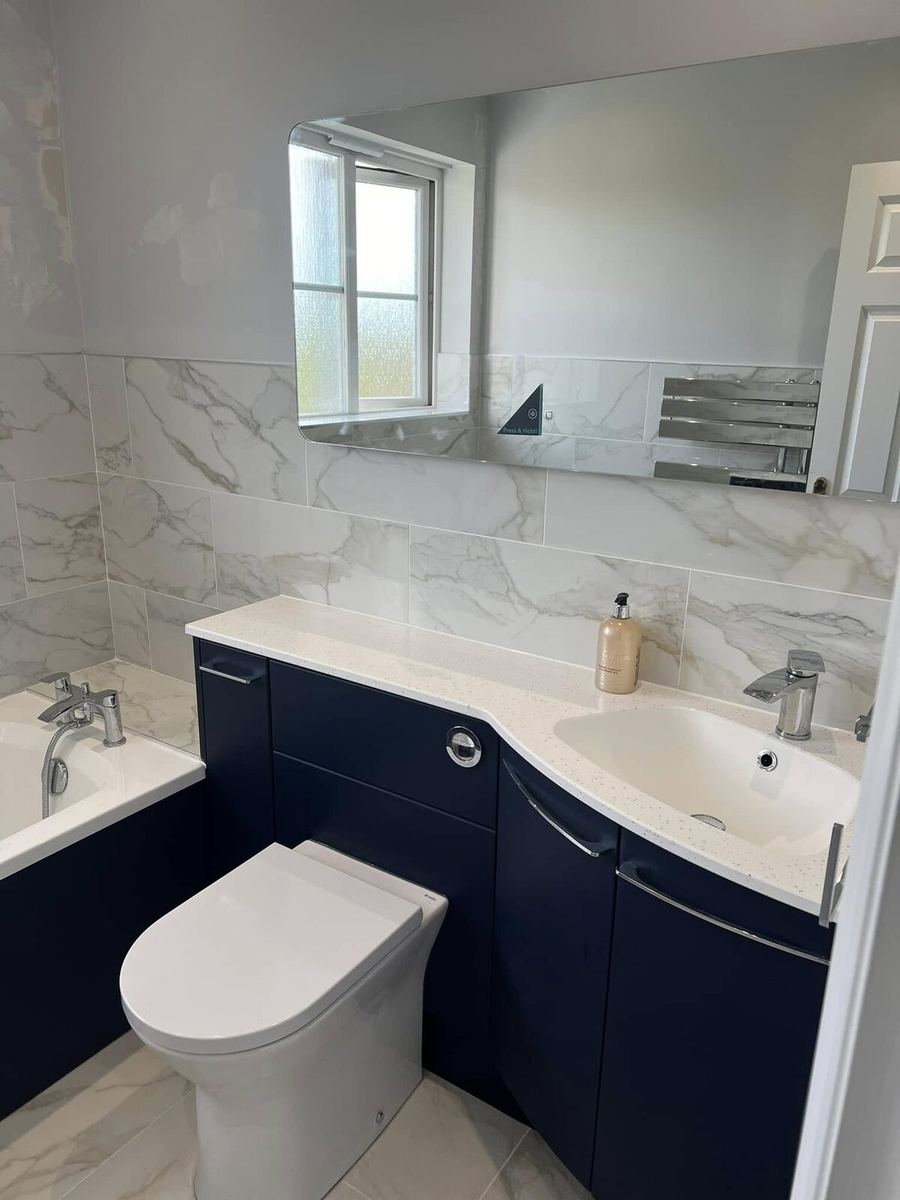 Bathroom with navy blue fitted vanity furniture, curved basin, concealed cistern WC and marble-effect wall tiling