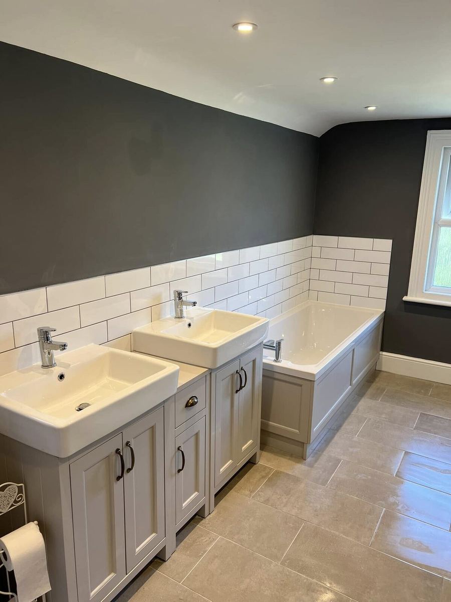 Family bathroom with two square basins set into painted shaker-style units, a panelled bath surround and white metro tiling