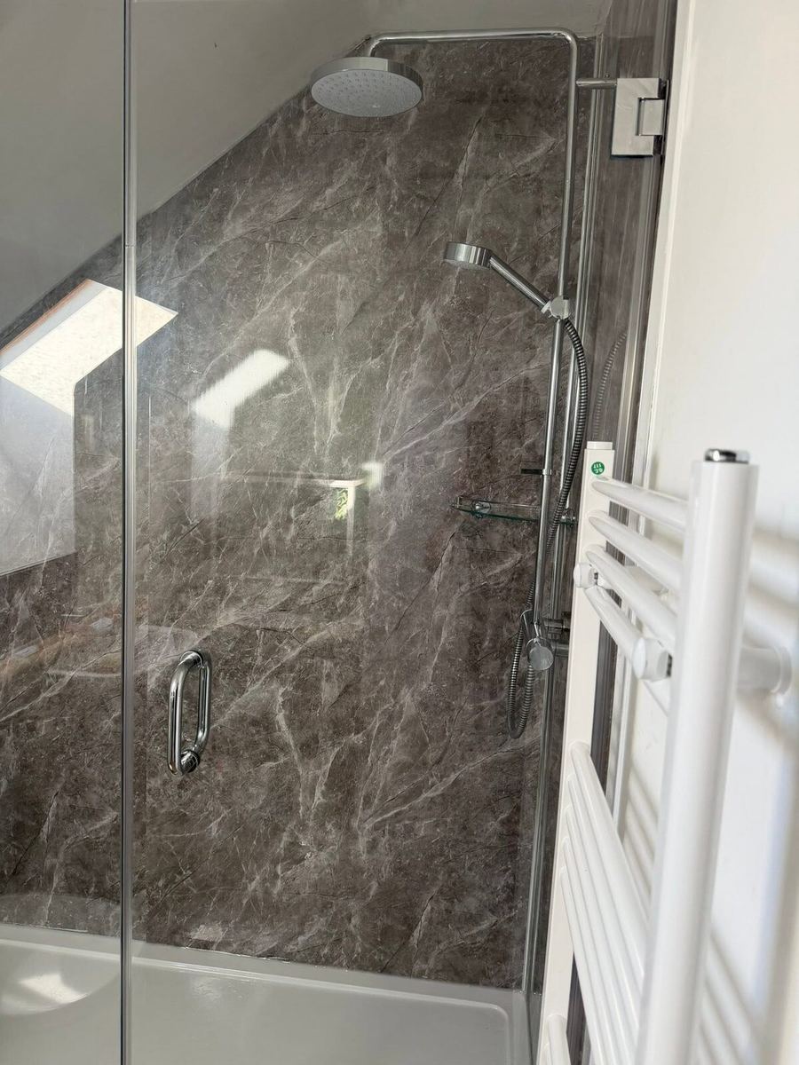 Shower enclosure with glass screen cut at an angle to fit beneath a sloping loft ceiling, lined with dark grey marble-effect tiling