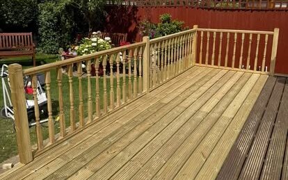 Raised timber deck in treated softwood with grooved boards and a turned spindle balustrade, overlooking a garden