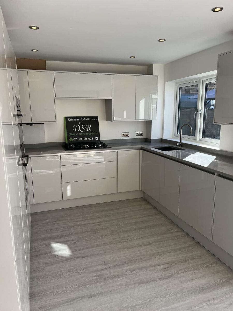 Completed kitchen with handleless gloss units, dark grey worktops, gas hob and wood-effect plank flooring